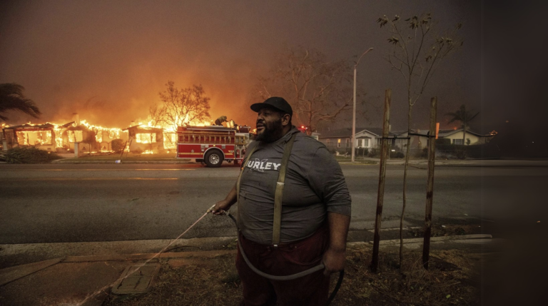 A resident sprays their property with a garden hot as the Eaton fire engulfs structure across the street, in Altadena, California. (AP Photo/Etham Swope)